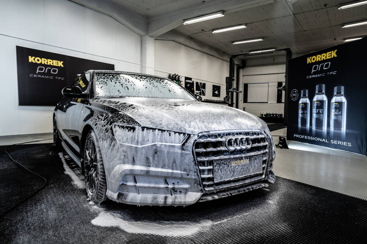 Mustaa autoa pestään ammattilaisen toimesta runsaalla vaahdolla KORREK Pro -keskuksessa, jossa näkyy kotimaiset tuotteet taustalla.
